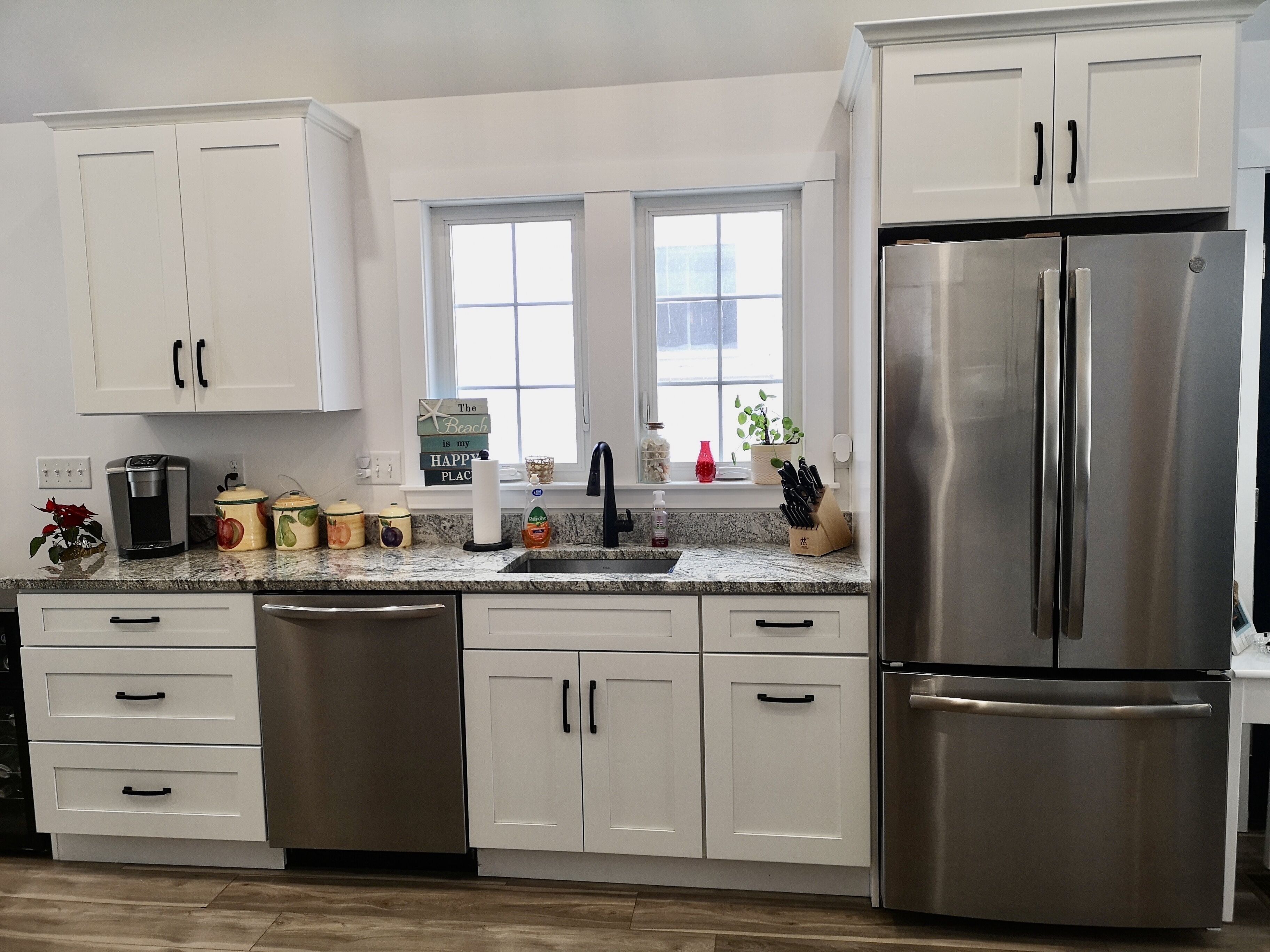 A modern kitchen with white cabinets, a stainless steel refrigerator, and a granite countertop.