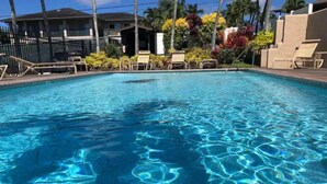 Une piscine d’un bleu éclatant, dont on peut voir les ondulations à la surface, entourée de chaises longues et de palmiers.