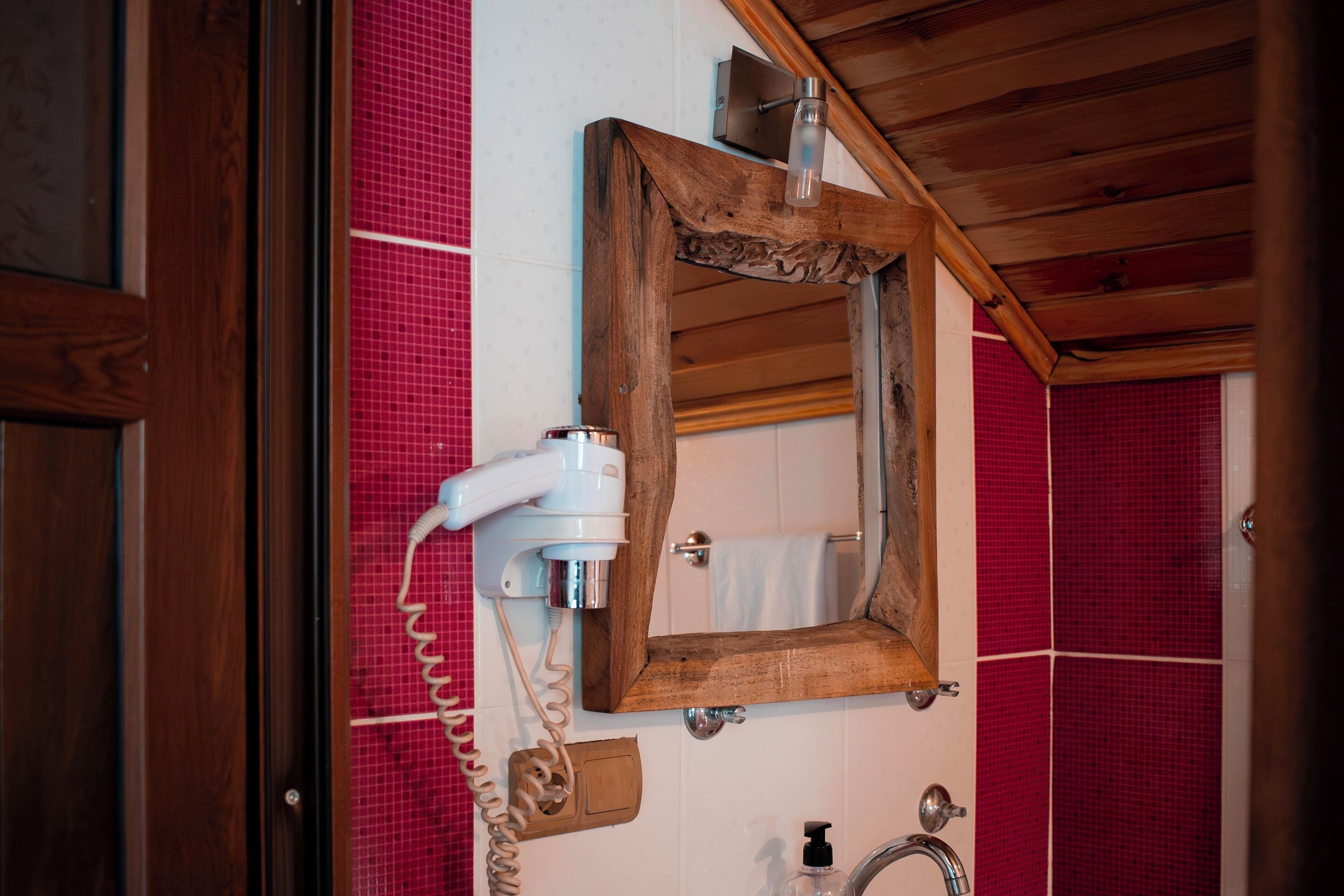 A bathroom with a wooden ceiling, a mirror, a hairdryer, and red-tiled walls.
