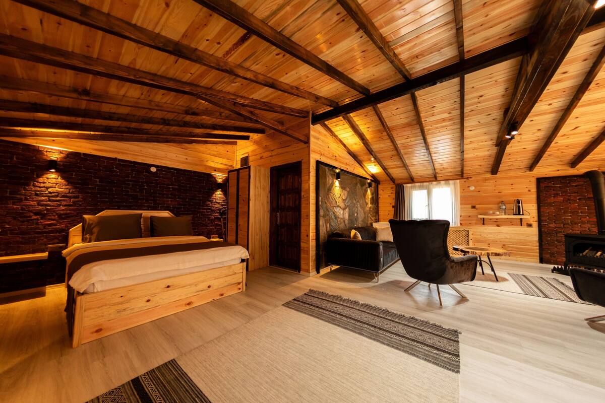 A wooden interior with a bed, a sofa, a fireplace, and a dining area.