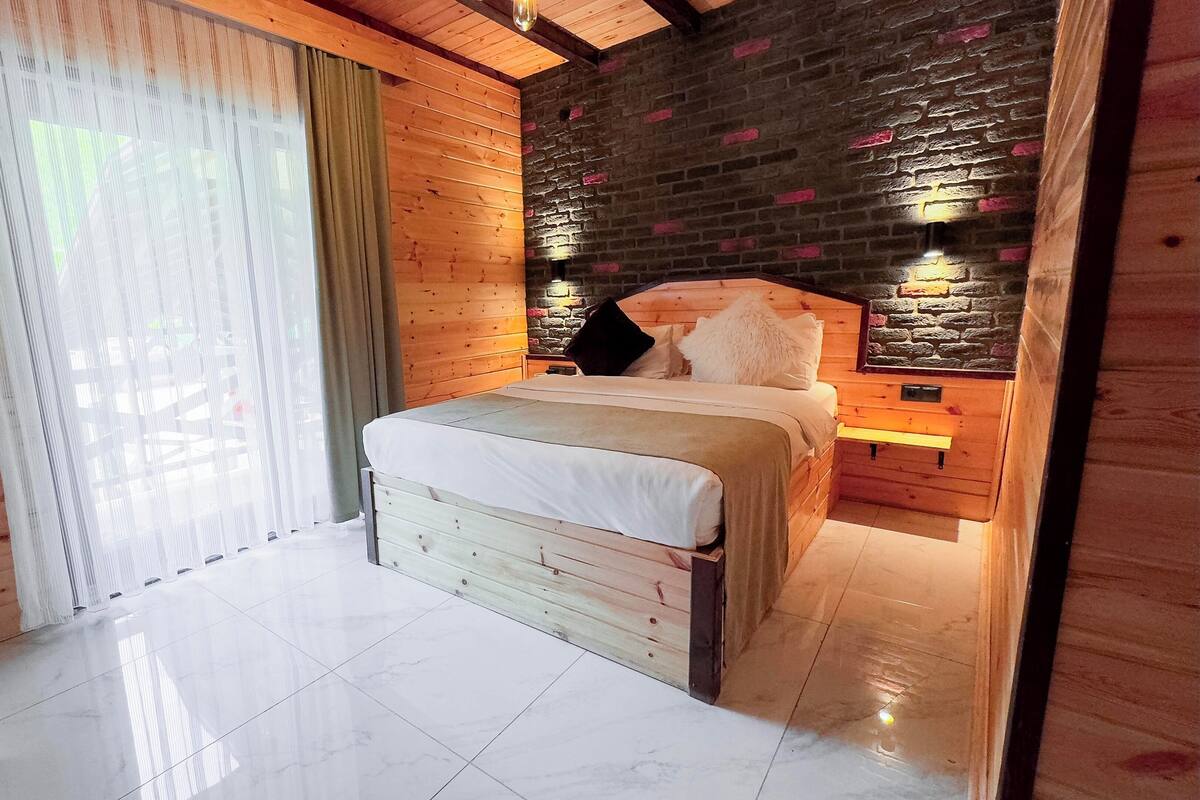 A wooden room with a bed, a stone wall, and a window with curtains.