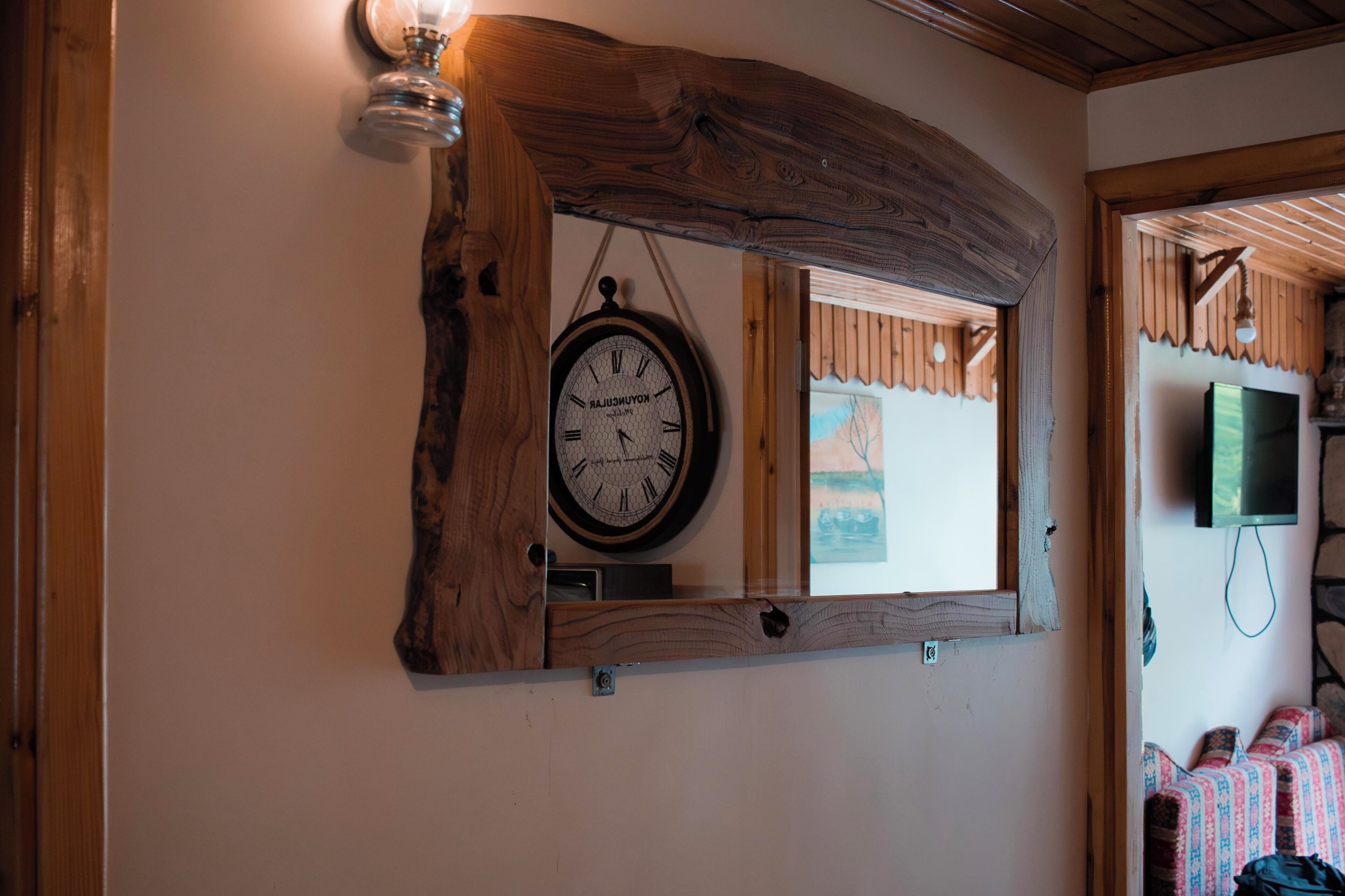 A rustic wooden beam ceiling, a wall-mounted clock, and a window with a view of the outside.