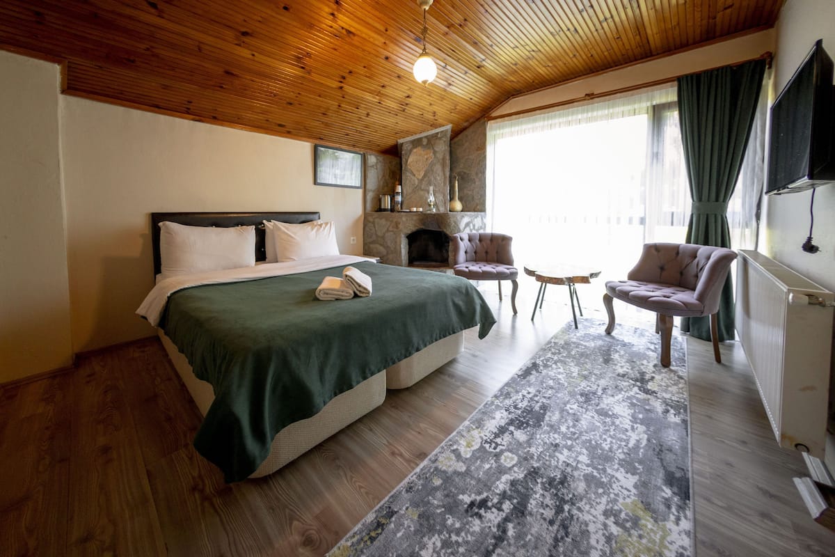A bedroom with a bed, a fireplace, two chairs, and a large window with curtains.