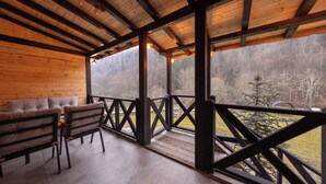 Terraza de madera con sofá y sillas, con vistas a un área boscosa.