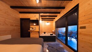 Un dormitorio de cabaña de madera con una cama grande, una bañera y vistas al exterior a través de una puerta corrediza de vidrio.