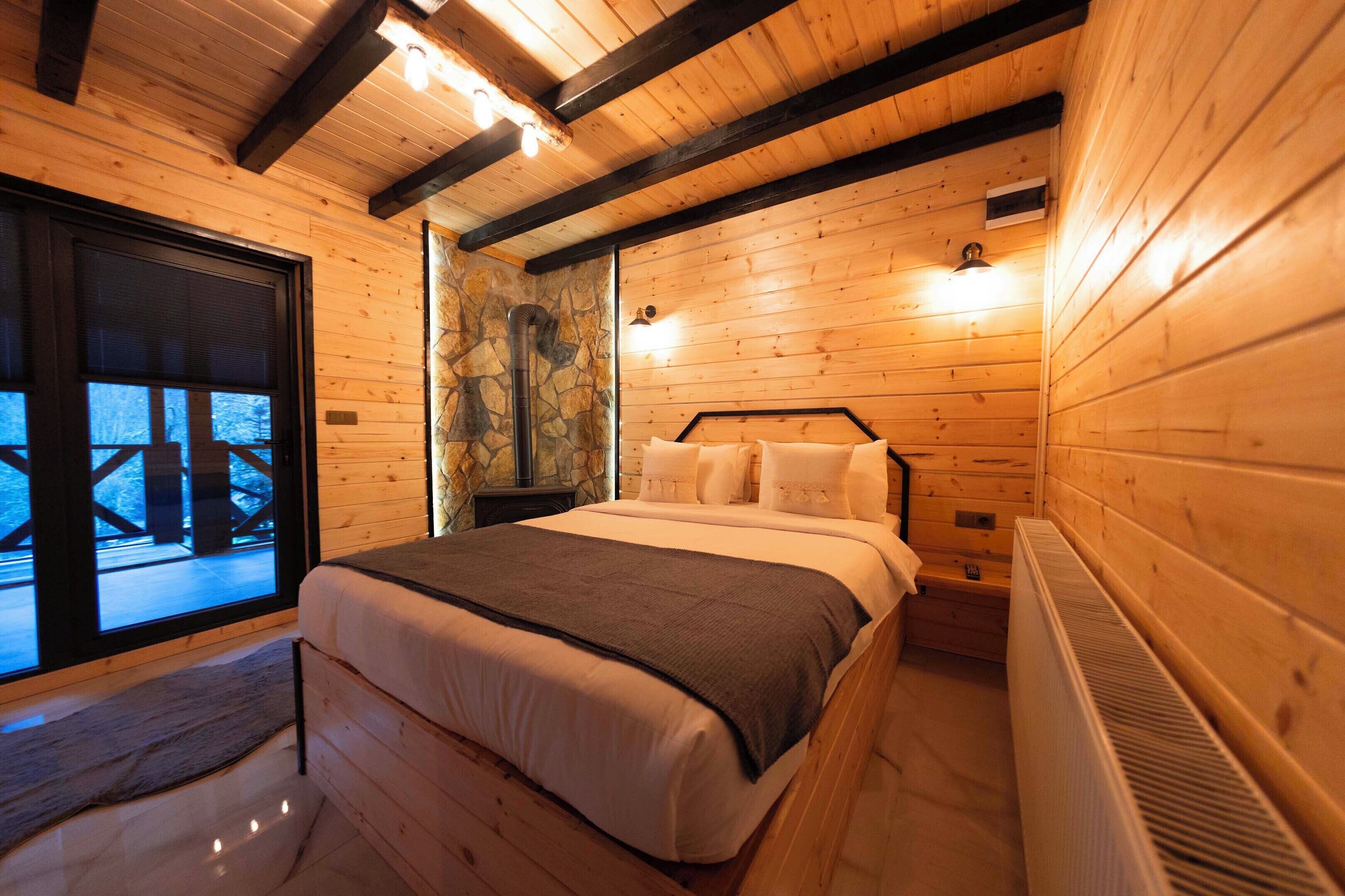 A wooden cabin bedroom with a bed, a stone wall, and a view through a glass door.