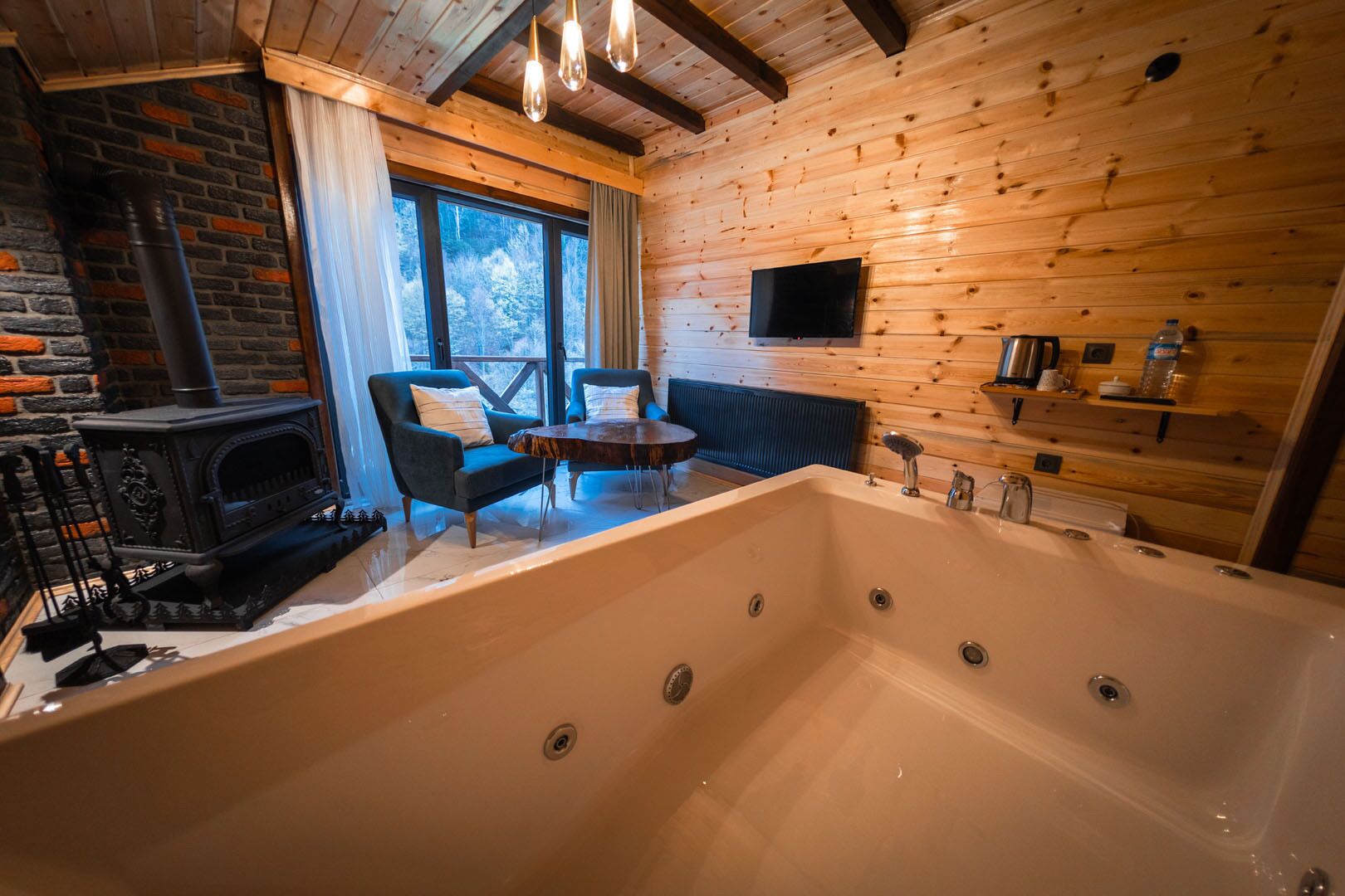 A wooden cabin interior with a large bathtub, a fireplace, and a TV mounted on the wall.
