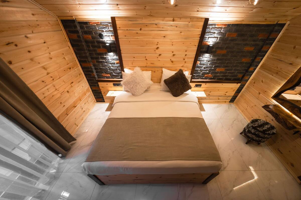 A cozy room with a large bed, wooden walls, and a stone fireplace.