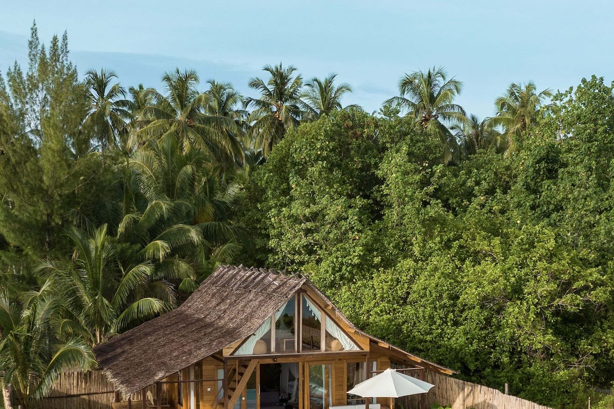 A wooden house with a thatched roof, a swimming pool, and a wooden deck.