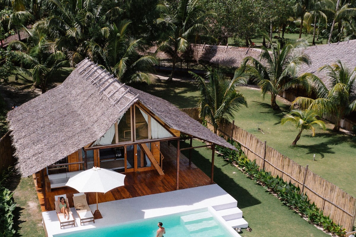 A house with a swimming pool, surrounded by palm trees and a wooden deck.