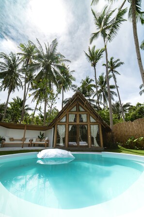 A swimming pool with a wooden deck and a glass-enclosed structure with a triangular roof.