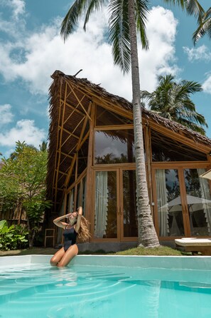 A poolside area with a thatched-roof structure, palm trees, and a clear sky. - Awera Resort & Spa (Pototogat Island)