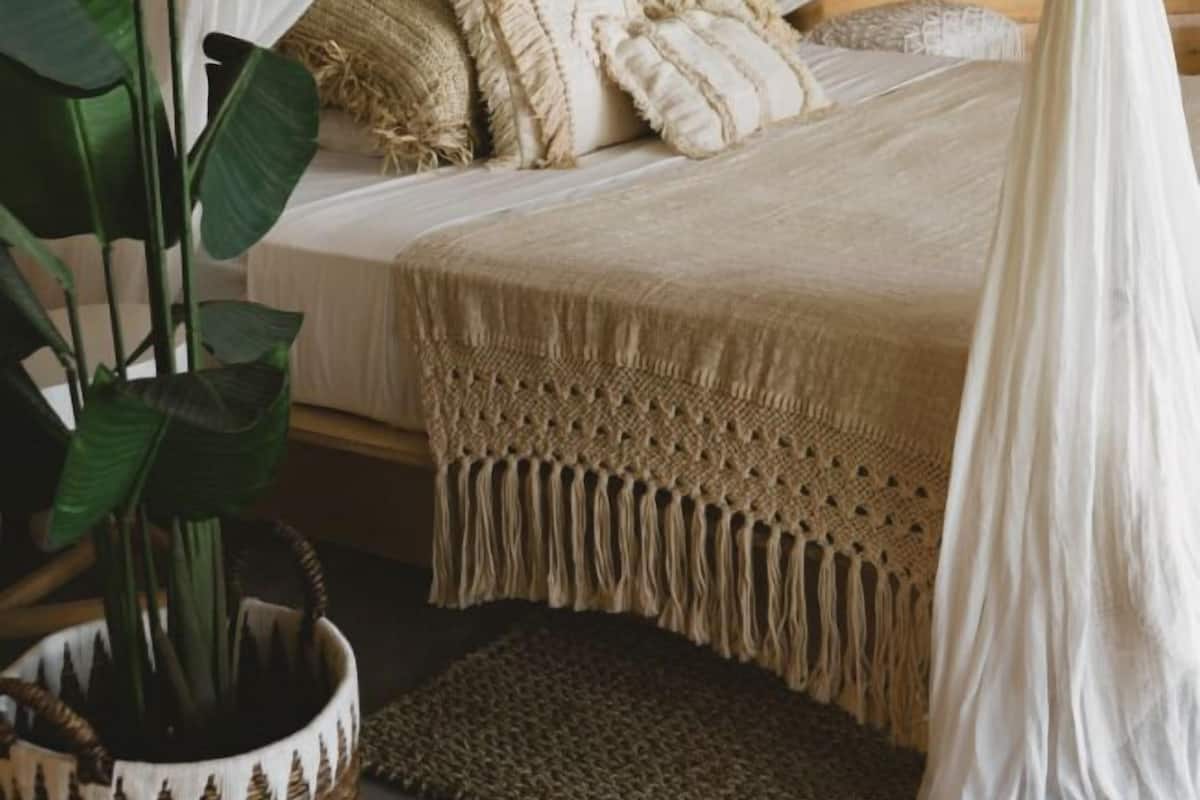A bedroom with a canopy bed, a woven basket with a plant, and a textured rug.