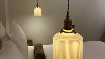 Una habitación de hotel con una lámpara colgante grande y acanalada de color blanco, otra lámpara colgante más pequeña también blanca, y una toalla enrollada sobre la cama.