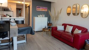 A modern living room with a red sofa, a dining table with chairs, a white cabinet, and decorative mirrors on the wall. - T2 Large terrace with sea view & direct access to the beach – Collioure sector (Port-Vendres)