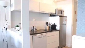 A compact kitchen with white cabinets, a dishwasher, a microwave, and a refrigerator. - T2 Large terrace with sea view & direct access to the beach – Collioure sector (Port-Vendres)