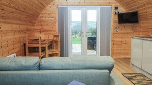 Een gezellige kamer met houten lambrisering, een bank, een eettafel en een aan de muur bevestigde televisie.