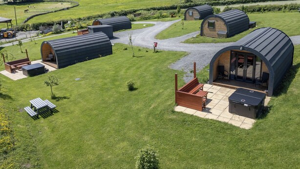 Een landelijke omgeving met meerdere kleine, gebogen-dak huisjes, elk met een terras en uitzicht op het omliggende groene landschap.