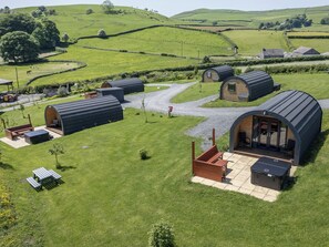 A rural setting with multiple small, curved-roofed cabins, each with a patio area and a view of the surrounding green landscape.