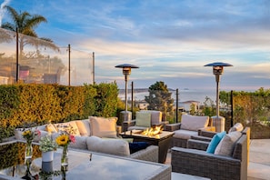 An outdoor seating area with wicker furniture, a fire feature, and a view of the ocean.