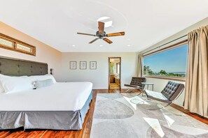 A hotel room with a large bed, a ceiling fan, a view of the outdoors, and a seating area with a table.