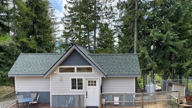 A small, single-story cabin with a gabled roof, a front door, and a deck with outdoor seating.