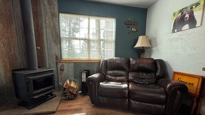 A living room with a leather sofa, a fireplace, a window with blinds, and a bear picture on the wall.