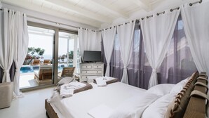 A bedroom with a large bed, a television, a dresser, and a view of an outdoor pool and landscape. - Villa Olympia - a palm trees paradise in front of the sea. (Heraklion Crete)