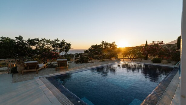 A swimming pool with a view of the sunset, surrounded by lounge chairs and plants. - Villa Olympia - a palm trees paradise in front of the sea. (Heraklion Crete)