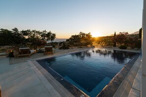 A swimming pool with a view of the sunset, surrounded by lounge chairs and plants.