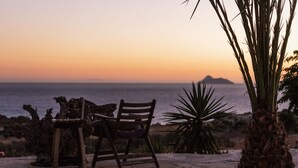 A wooden bench and chair on a stone patio overlooking the ocean at sunset. - Villa Olympia - a palm trees paradise in front of the sea. (Heraklion Crete)