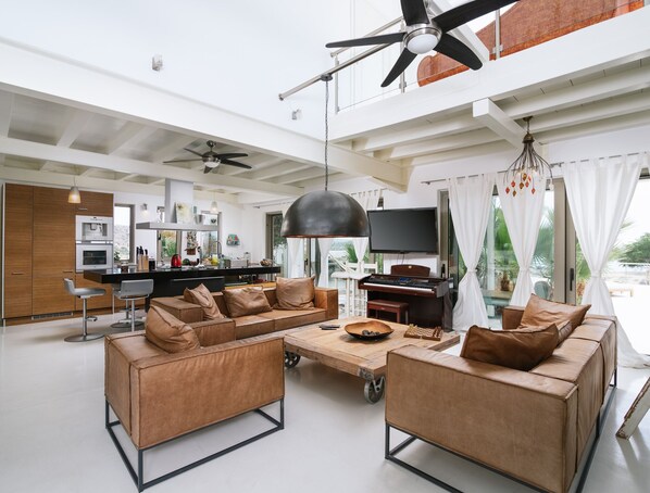 A spacious living area with a modern kitchen, a large ceiling fan, and a flat-screen TV.