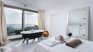A modern hotel room with a large window, a black bathtub, a bed with neatly folded towels, and a mirror. - Villa Olympia - a palm trees paradise in front of the sea. (Heraklion Crete)