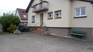 A building with a staircase leading to a balcony, a bench, and outdoor seating. - Vacation home rental near Colmar (Wickerschwihr)