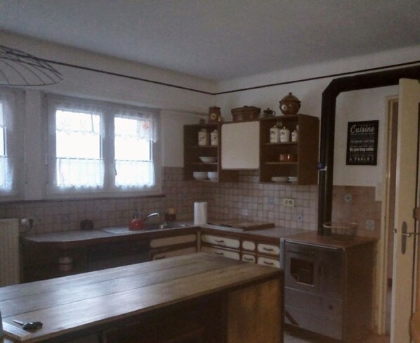 A kitchen with a wooden countertop, cabinets, and a stove. There are windows with curtains, a sink, and a sign on the wall.