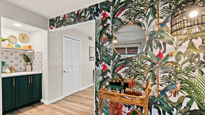 Una habitación con papel tapiz de temática tropical, una mesa de centro de madera con bebidas y un espejo.
