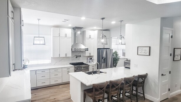 A modern kitchen with white cabinetry, a central island with bar stools, stainless steel appliances, and pendant lighting. - Historic Hyde Park Village Haven (Tampa)