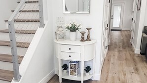 A modern hallway with a wooden floor, a white console table with decorative items, a mirror, and a staircase with metal railings. - Historic Hyde Park Village Haven (Tampa)