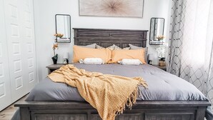 A bedroom with a dark wood headboard, a large bed with multiple pillows, a throw blanket, bedside tables with lamps, and wall-mounted mirrors. - Historic Hyde Park Village Haven (Tampa)