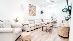 A modern living room with a beige sectional sofa, a small round coffee table, and a wicker side table. - Historic Hyde Park Village Haven (Tampa)