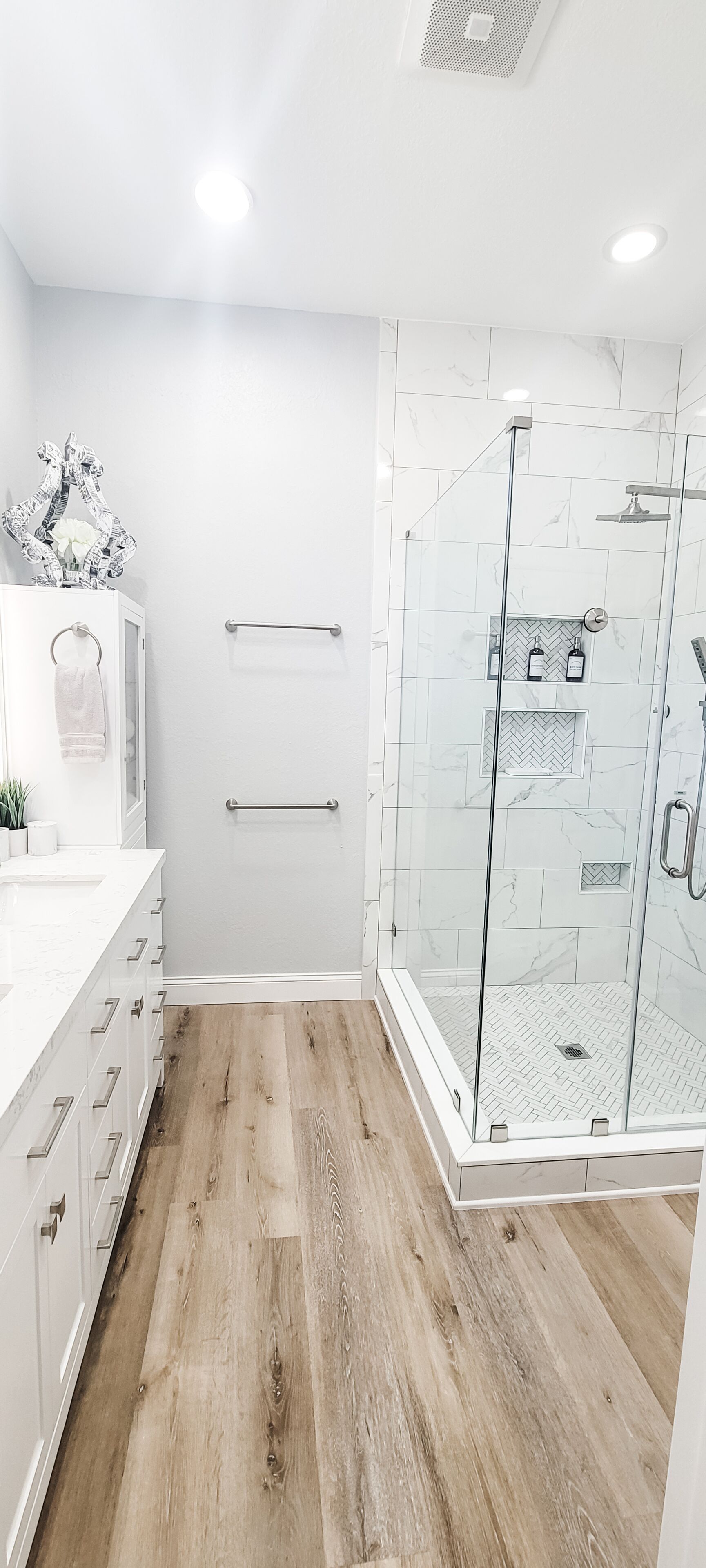 Un baño moderno con ducha, muebles blancos y suelo con diseño en espiga.