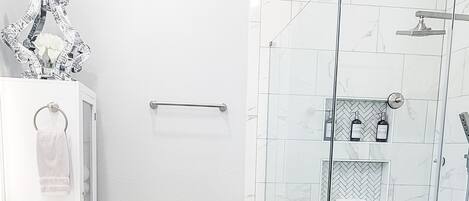 Un baño moderno con ducha, muebles blancos y suelo con diseño en espiga.