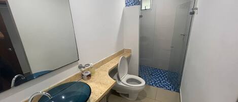 A bathroom with a blue sink, white toilet, and a shower area with blue tiles.