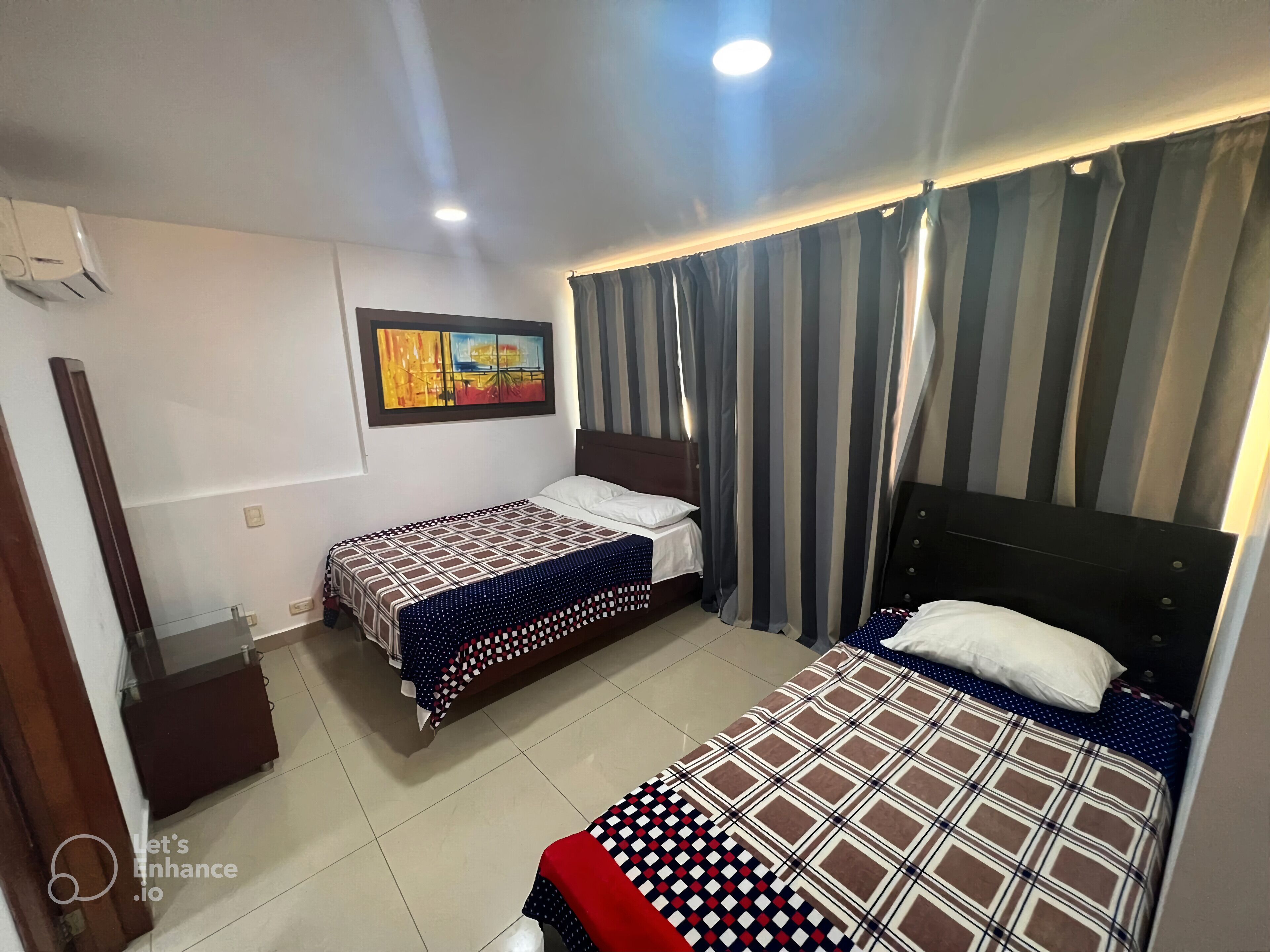 A hotel room with two beds, a painting on the wall, and striped curtains.