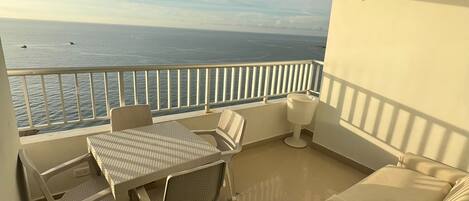 A balcony with a view of the sea, a table with chairs, and a sofa.