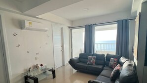 Un salon avec un canapé, une table basse en verre et une porte coulissante donnant sur un balcon.