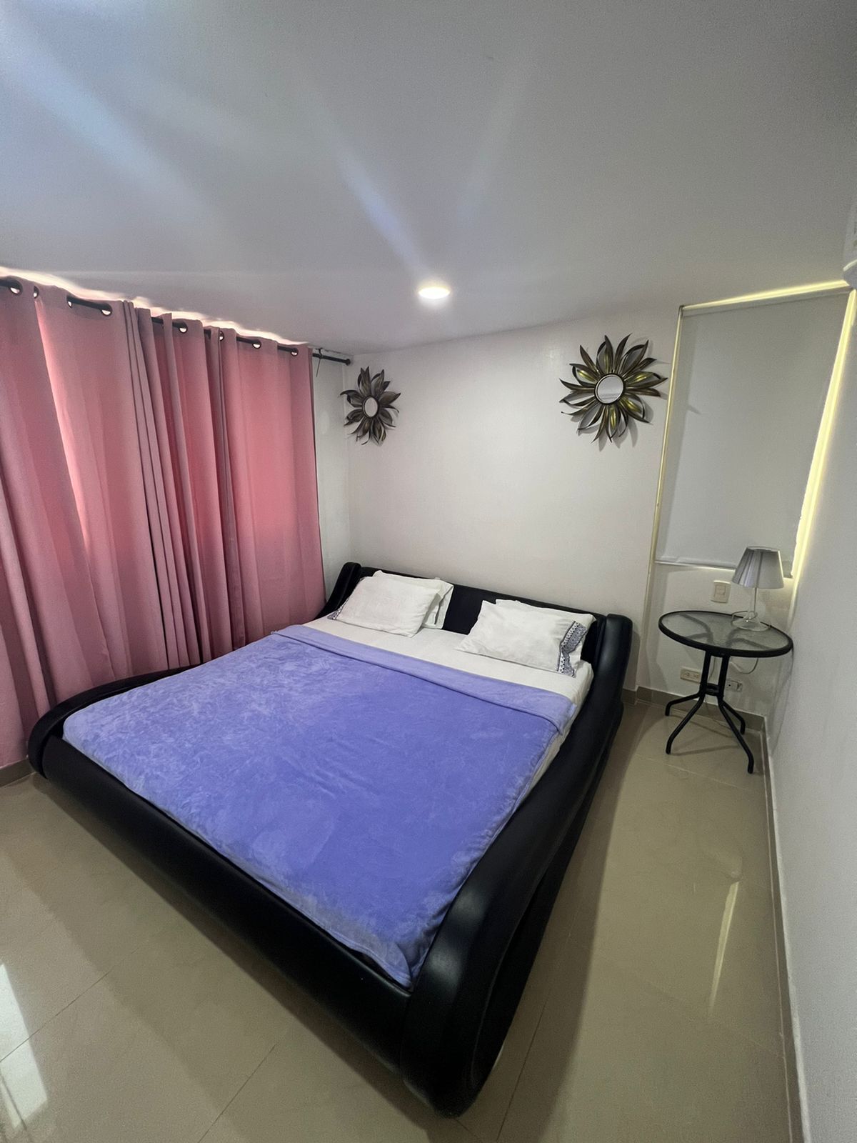 A bedroom with a bed, curtains, a small table, and wall decorations.