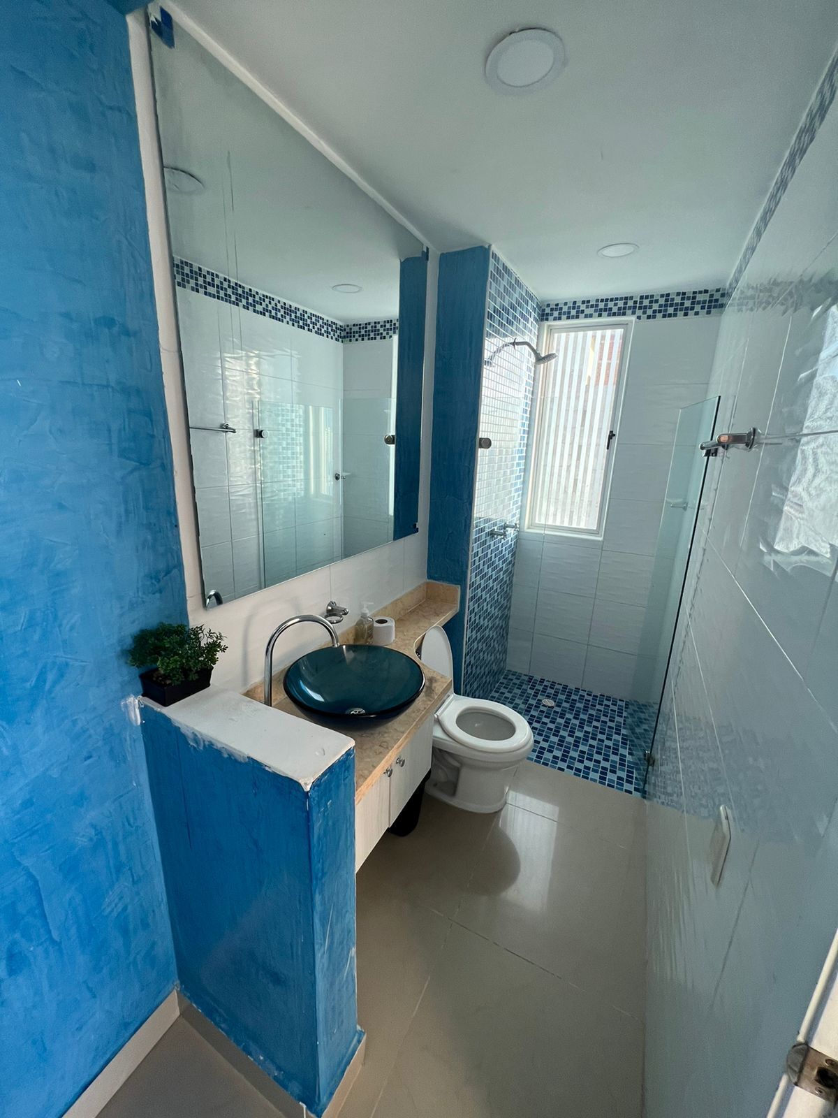 A bathroom with a blue and white tiled design, a glass shower enclosure, and a sink with a blue basin.