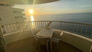 Un balcon avec une table et des chaises, offrant une vue sur la mer au coucher du soleil.