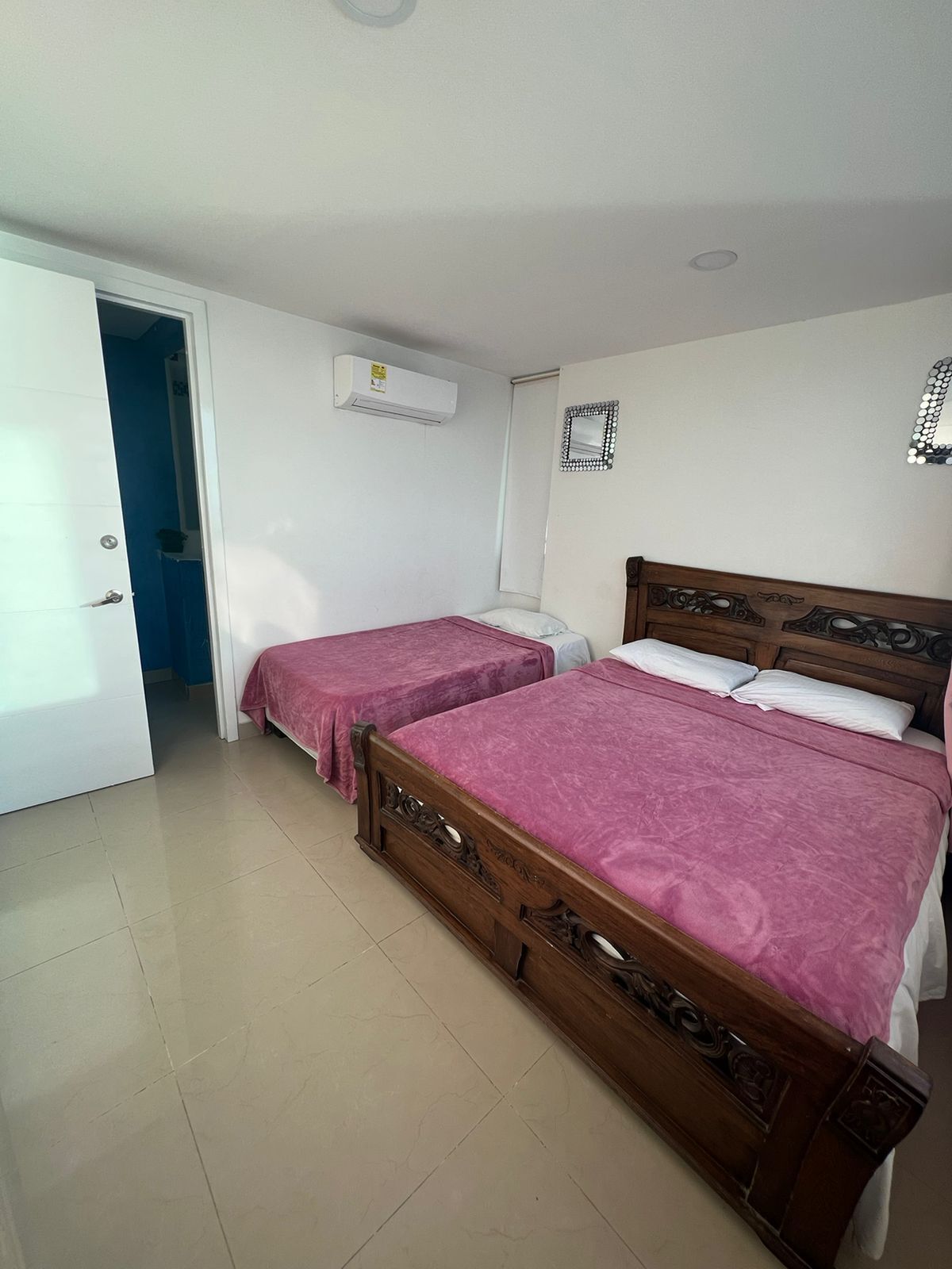 A bedroom with two beds, a white door, an air conditioning unit, and a mirror on the wall.